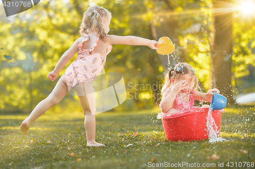 Image of The cute little blond girls playing with water splashes on the field in summer