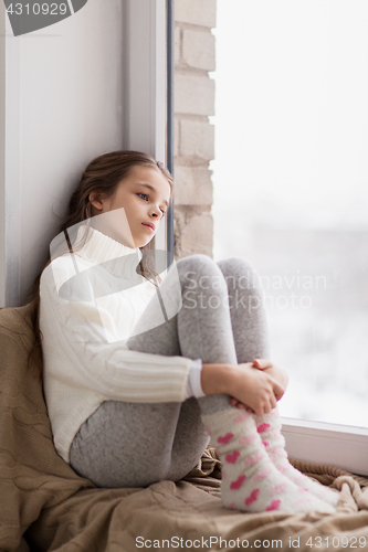 Image of sad girl sitting on sill at home window in winter