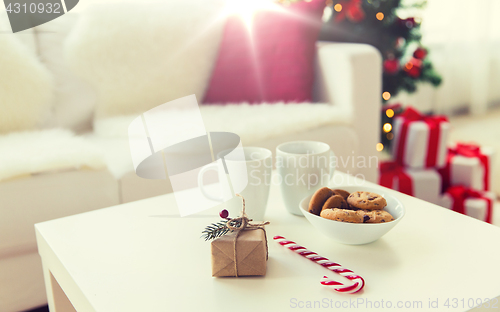 Image of close up of gift, sweets and cups on table at home