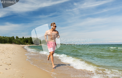 Image of happy man with headphones running along beach