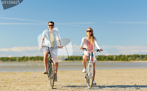 Image of happy young couple riding bicycles at seaside