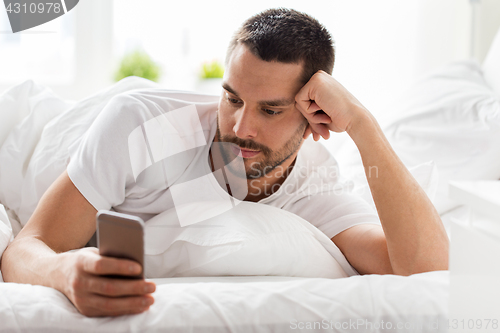 Image of young man with smartphone in bed in morning