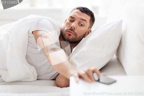 Image of young man reaching for smartphone in bed