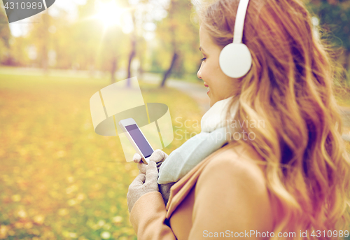 Image of woman with smartphone and earphones in autumn park