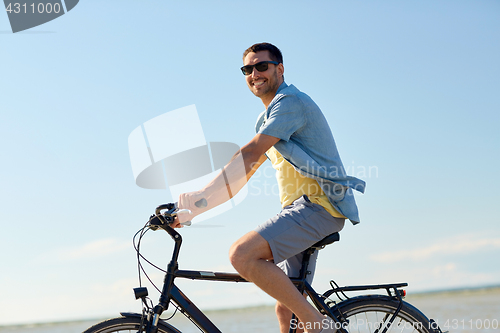 Image of happy man riding bicycle along summer beach