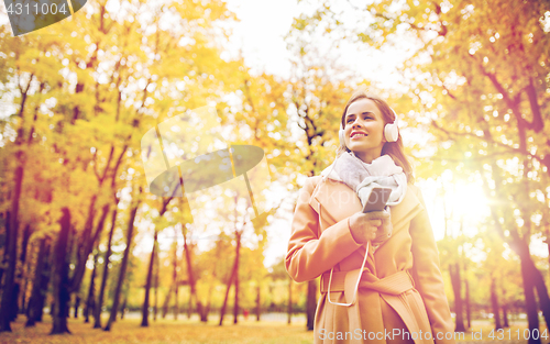 Image of woman with smartphone and earphones in autumn park
