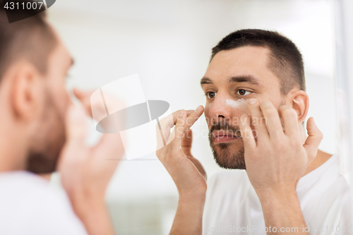 Image of young man applying cream to face at bathroom