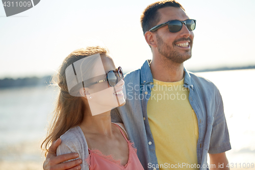 Image of happy couple in sunglasses hugging on summer beach
