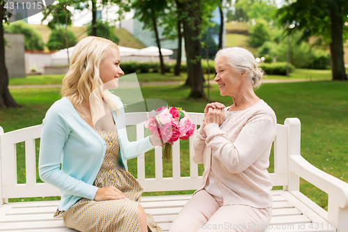 Image of daughter giving flowers to senior mother at park