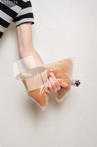 Image of hand holding plastic bag with tap full of apple juice