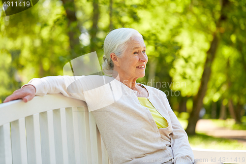 Image of happy senior woman sitting on bench at summer park