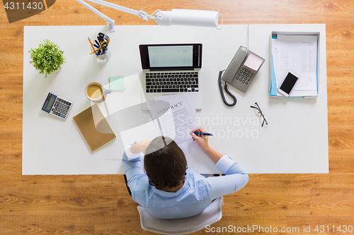 Image of businesswoman signing contract document at office