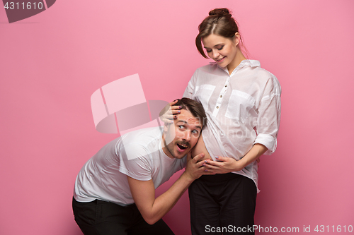 Image of Handsome man is listening to his beautiful pregnant wife\'s tummy and smiling