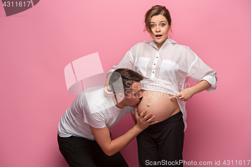 Image of Handsome man is listening to his beautiful pregnant wife\'s tummy and smiling