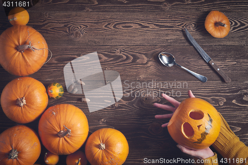 Image of Hands holding Halloween pumpkin over wooden background