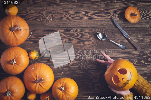 Image of Hands holding Halloween pumpkin over wooden background