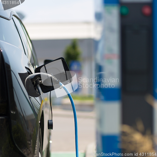 Image of Power supply plugged into an electric car being charged.
