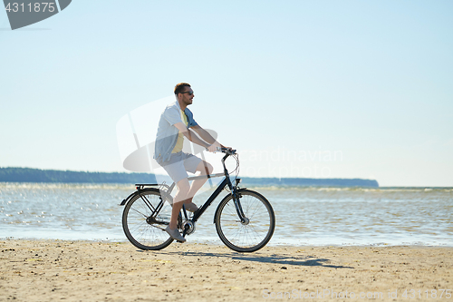 Image of happy man riding bicycle along summer beach