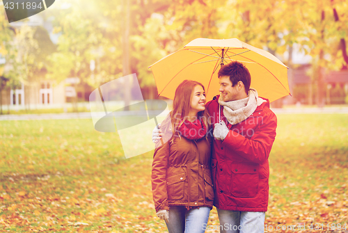 Image of smiling couple with umbrella in autumn park