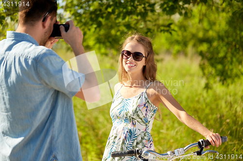 Image of man photographing woman with bicycle by camera
