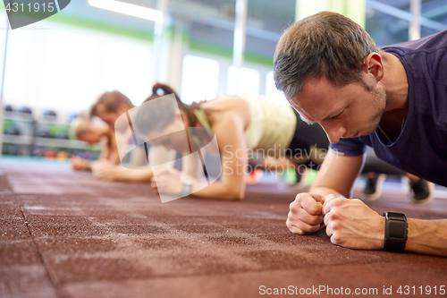 Image of man at group training doing plank exercise in gym