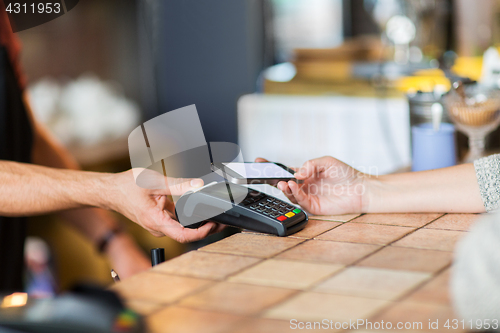Image of hands with payment terminal and smartphone at bar