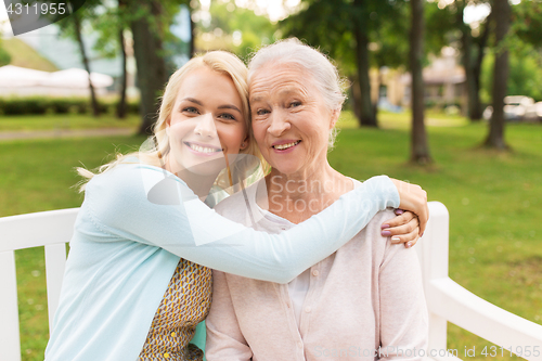 Image of daughter with senior mother hugging on park bench