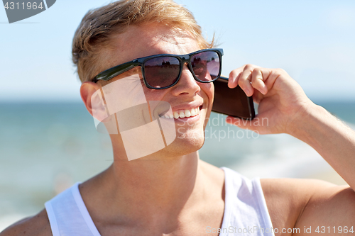 Image of smiling man calling on smartphone on summer beach