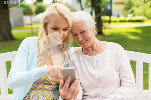 Image of daughter and senior mother with smartphone at park