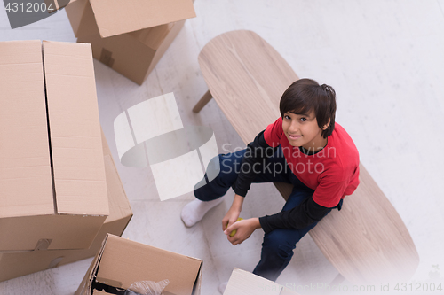 Image of boy sitting on the table with cardboard boxes around him top vie