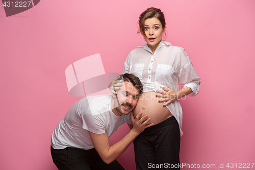 Image of Handsome man is listening to his beautiful pregnant wife\'s tummy and smiling