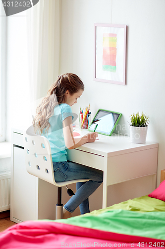 Image of girl with tablet pc writing to notebook at home