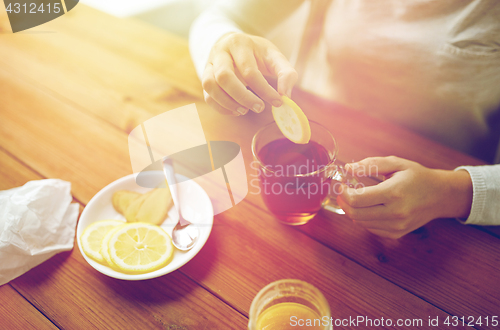 Image of close up of woman adding lemon to tea cup