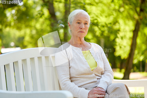 Image of sad senior woman sitting on bench at summer park