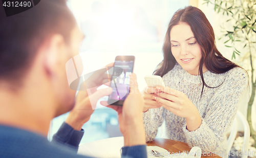 Image of happy couple with smartphones drinking tea at cafe