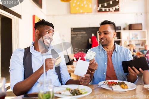 Image of happy friends with money paying bill at restaurant