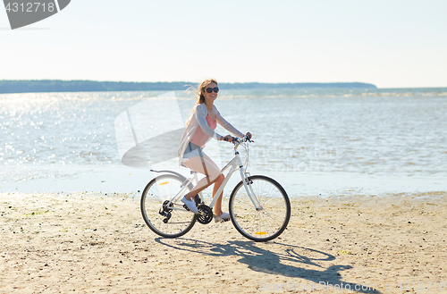 Image of happy woman riding bicycle along summer beach