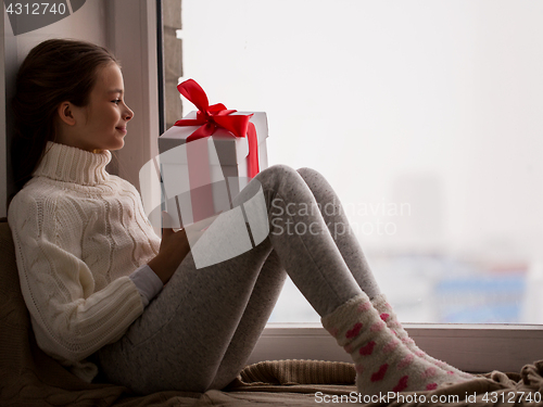 Image of girl with gift sitting on sill at home window