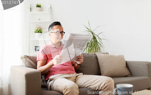 Image of asian man in glasses reading newspaper at home
