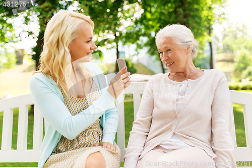 Image of daughter and senior mother with smartphone at park