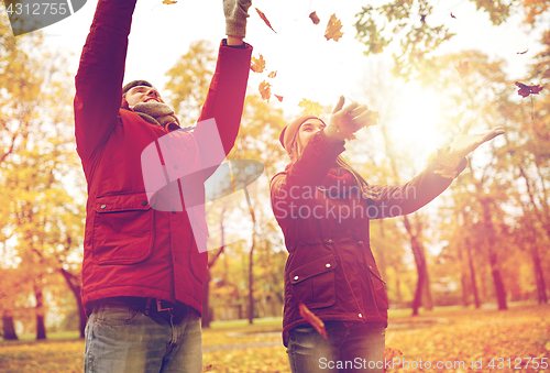 Image of happy young couple throwing autumn leaves in park
