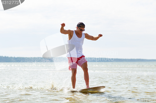 Image of young man riding on skimboard on summer beach