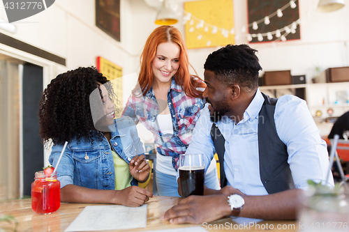 Image of happy friends with drinks at bar or restaurant