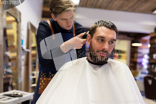 Image of man and barber with trimmer cutting hair at salon