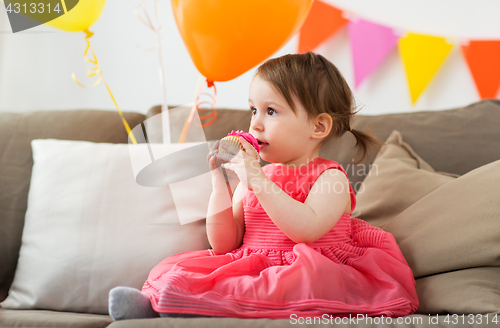 Image of happy baby girl eating cupcake on birthday party