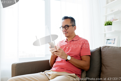 Image of asian man with smartphone sitting on sofa at home