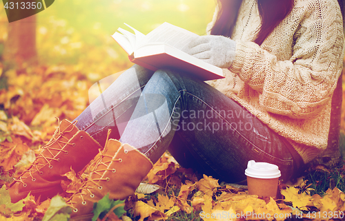 Image of woman with book drinking coffee in autumn park