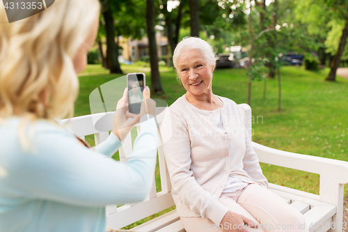 Image of daughter photographing senior mother by smartphone