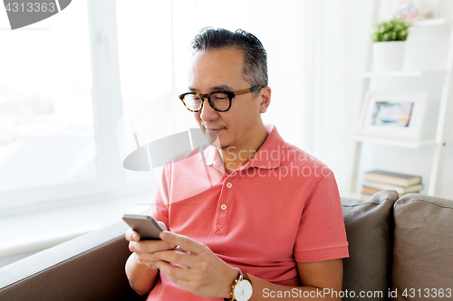 Image of asian man with smartphone sitting on sofa at home