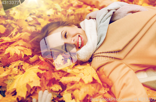 Image of beautiful happy woman lying on autumn leaves